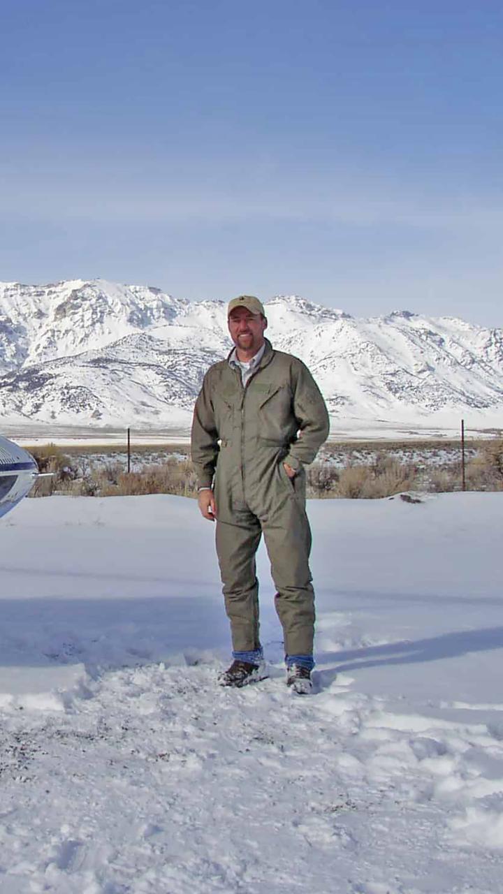 Tony Wasley in mountainous winter landscape standing beside a helicopter